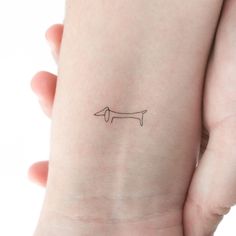 a small dachshund tattoo on the left wrist is shown in black ink