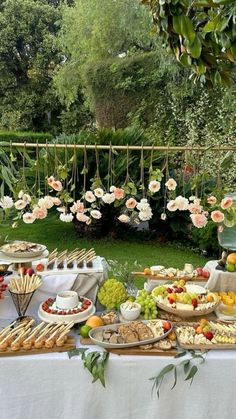 a table filled with lots of food on top of a lush green field next to trees