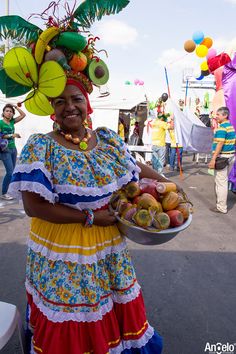 a woman in a colorful dress holding a bowl of fruit