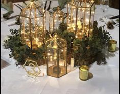 there are many lanterns that have lights in them on the table with greenery and candles