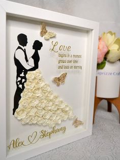 a white frame with some flowers and a couple in wedding attire on top of it