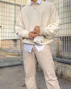 a man standing in front of a fence with his hands on his hips wearing a white sweater and khaki pants