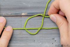 two hands are tying a green string to a piece of wood with one hand and the other