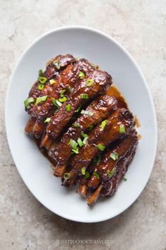 a white plate topped with meat covered in sauce and scallions on top of a table