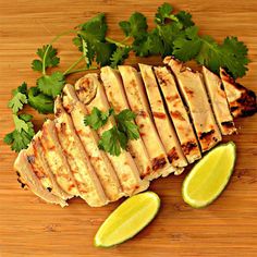 sliced chicken with cilantro and parsley on a cutting board next to lime wedges