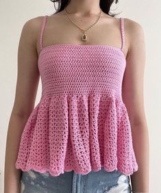 a woman wearing a pink crochet top and denim shorts with her hands in her pockets