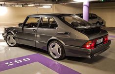 a car parked in a parking garage with purple stripes on the floor and two other cars behind it