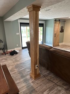 a living room with hard wood flooring and large wooden pillars in the middle of it