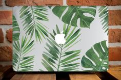 an apple laptop with green leaves painted on the cover, sitting on a wooden table in front of a brick wall