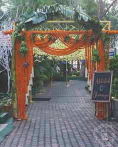 an orange and white wedding arch decorated with flowers, greenery and chalkboard sign