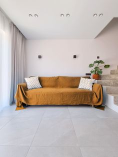 a couch sitting on top of a white floor next to a window with curtains and potted plants