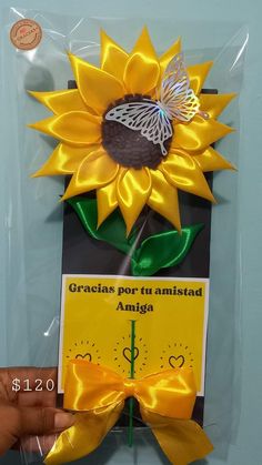 a hand holding a card with a sunflower on it and a ribbon attached to it