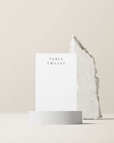 a piece of paper with the words table twelve on it sitting next to a rock