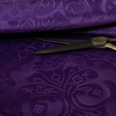 a pair of gold scissors sitting on top of a purple fabric with skulls and hearts