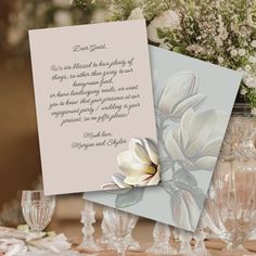 two cards with flowers on them sitting on a table next to wine glasses and vases