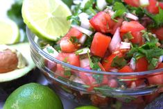 a salad with tomatoes, onions and cilantro in a glass bowl next to limes