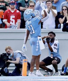 a football player is standing on the field with his arms in the air and people behind him