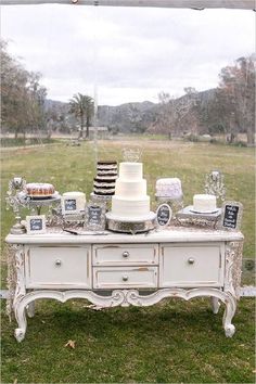 a table with cake and desserts on it sitting in the grass next to a field