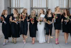 a group of women standing next to each other holding bouquets in front of a building