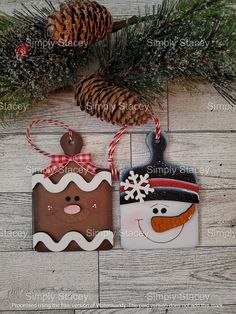 two christmas ornaments are hanging on a wooden surface with pine cones and evergreen branches in the background