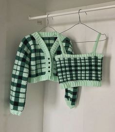 a green and white knitted sweater hanging on a clothesline with a button down shirt underneath it