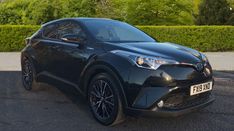 a black toyota c - hr is parked on the street in front of some bushes