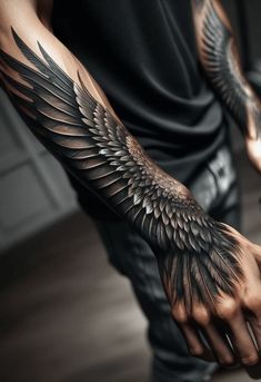 a man's arm with black and grey wings on his left hand, while he is wearing a black t - shirt