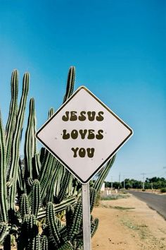 a sign that says jesus loves you next to a cactus