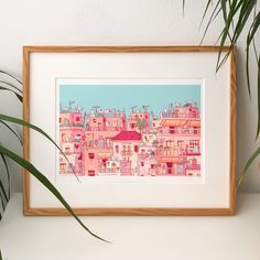 an art print of pink buildings with palm trees in the foreground and a potted plant next to it