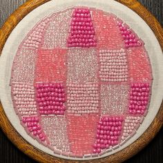 a close up of a embroidery on a wooden hoop with pink and white squares in it