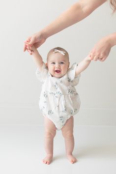 a baby in a white bodysuit holding her mother's hand with both hands