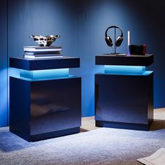 two black and blue tables with headphones on each one, in front of a blue wall