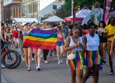 a group of people walking down a street holding a rainbow flag and cell phone in their hands