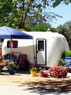 an rv parked under a blue tarp next to some flowers and potted plants