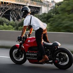 a man riding on the back of a red motorcycle down a street next to a bridge