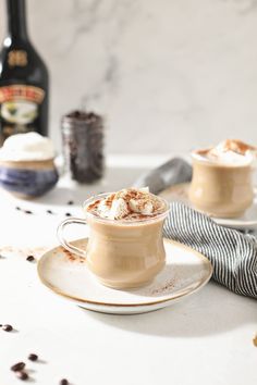 two cups filled with hot chocolate on top of a white plate next to a bottle of booze