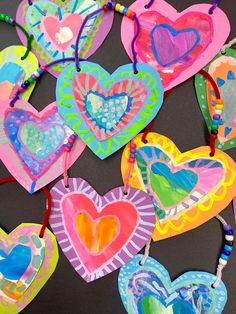 colorful paper hearts are hanging from strings on a black surface with beaded necklaces