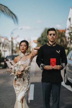 a man and woman standing next to each other in front of a car holding a red book