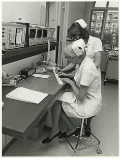 black and white photograph of two nurses working on an electronic device in the hospital room