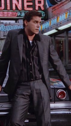 a man in a suit leaning on the hood of a car while standing next to a diner