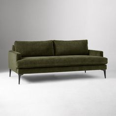 a green couch sitting on top of a white floor next to a gray wall in an empty room