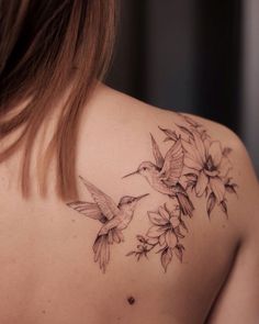 the back of a woman's shoulder with hummingbirds and flowers tattoo on it