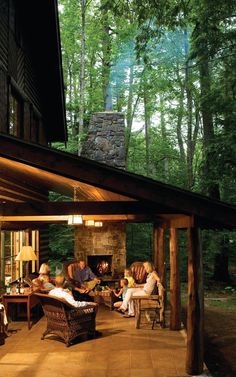 people are sitting on the porch in front of a log cabin with an open fire place