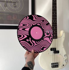 a person holding up a pink and black frisbee next to a bass guitar