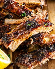 barbecue ribs and lemon wedges on a cutting board with sauce, seasoning and herbs