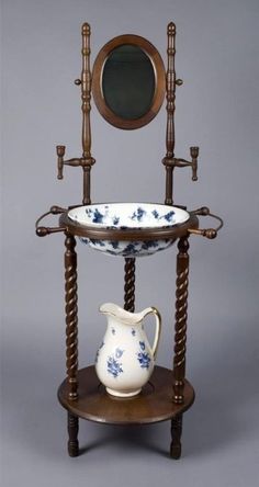 an antique wooden stand with a tea pot and mirror on the top, next to a vase