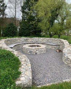 a stone fire pit surrounded by grass and trees