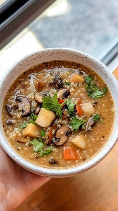 a hand holding a bowl of soup with mushrooms, carrots and spinach in it