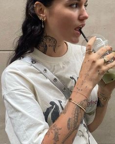 a woman with tattoos on her arm drinking from a cup and holding a straw in her hand