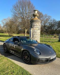 a grey sports car parked in front of a stone pillar and fenced in area